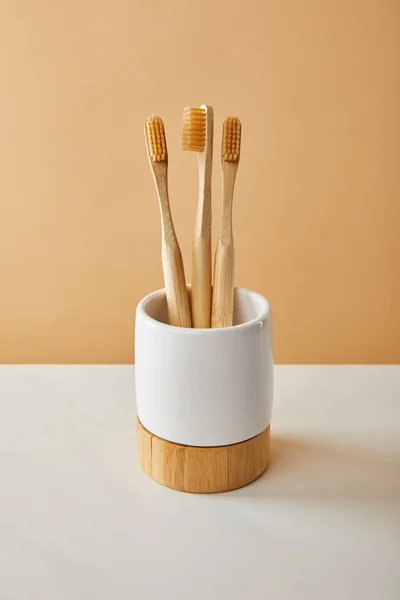 Cepillos de dientes de bambú marrón en soporte sobre mesa blanca y fondo beige — Stock Photo