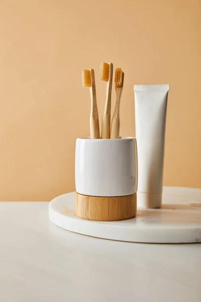 Pasta de dentes em tubo e suporte com escovas de bambu na superfície de mármore branco e fundo bege — Fotografia de Stock