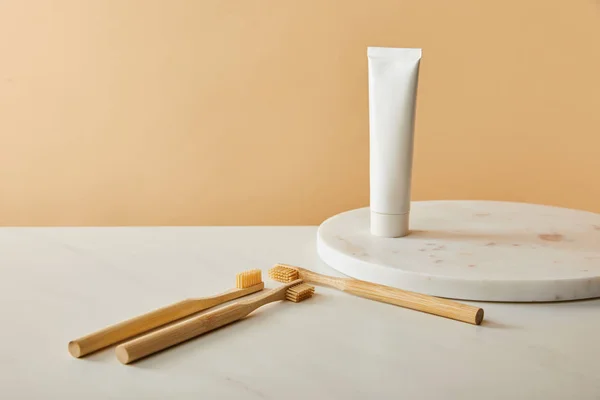 Tablero redondo de mármol con pasta de dientes en tubo y cepillos de dientes de bambú sobre mesa blanca y fondo beige - foto de stock