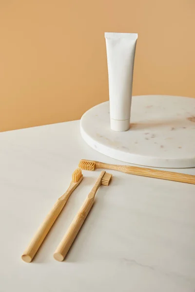Tablero redondo de mármol con pasta de dientes en tubo y cepillos de dientes de bambú sobre mesa blanca y fondo beige - foto de stock
