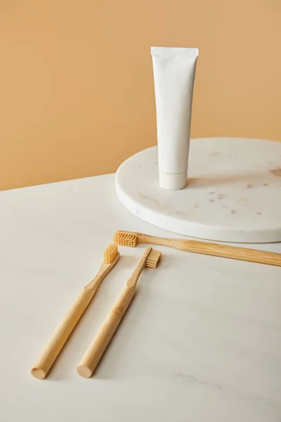 Marble round board with toothpaste in tube and bamboo toothbrushes on white table and beige background — Stock Photo