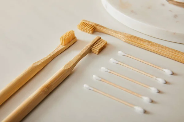 Tavola rotonda in marmo, spazzolini di bambù e auricolari su sfondo bianco — Foto stock