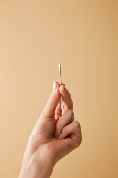 Vista recortada de la mano femenina sosteniendo el palo de la oreja sobre fondo beige - foto de stock