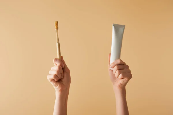 Abgeschnittene Ansicht einer Frau mit Bambus-brauner Zahnbürste und Zahnpasta in der Tube auf beigem Hintergrund — Stockfoto