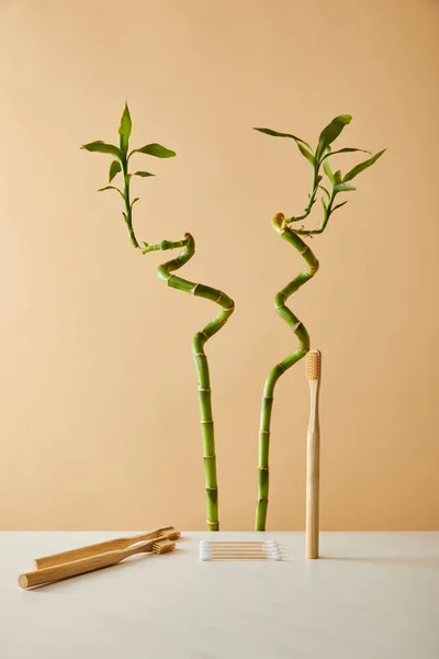 Bamboo toothbrush with ear sticks on white table and green bamboo on beige background — Stock Photo