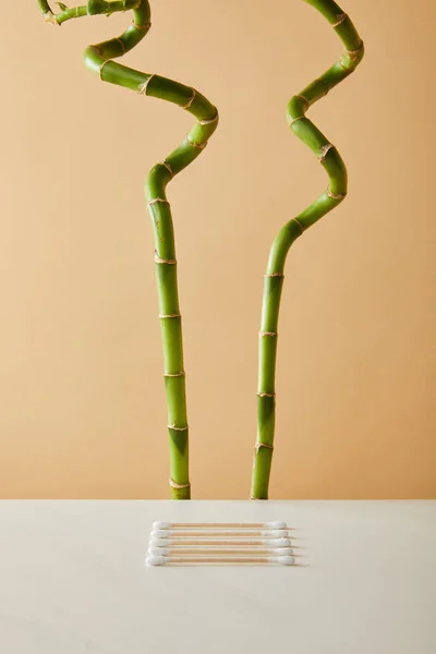 Ear sticks on white table with green bamboo on beige background — Stock Photo