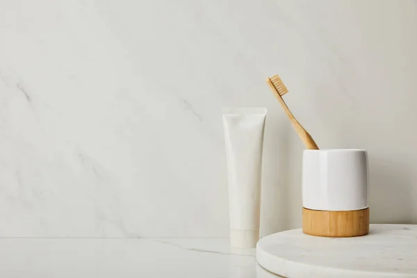 Holder with bamboo toothbrush and toothpaste in tube on white marble background — Stock Photo