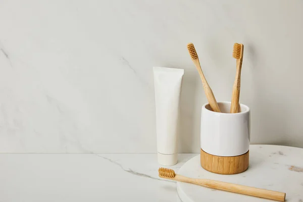 Cepillos de dientes de bambú, soporte y pasta de dientes en tubo sobre fondo de mármol blanco - foto de stock