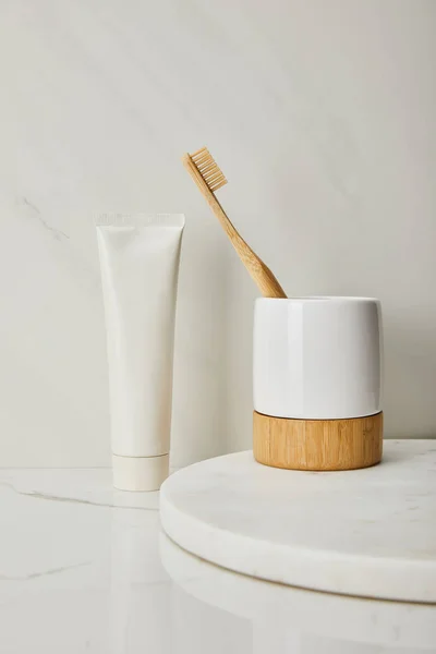 Soporte con cepillo de dientes de bambú y pasta de dientes en tubo sobre fondo de mármol blanco - foto de stock