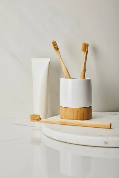 Bamboo toothbrushes, holder and toothpaste in tube on white marble background — Stock Photo