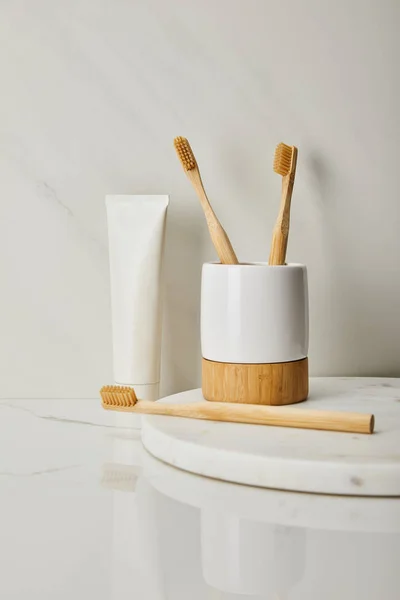 Cepillos de dientes de bambú, soporte y pasta de dientes en tubo sobre fondo de mármol blanco - foto de stock