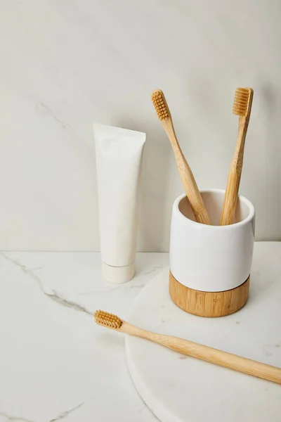 Toothpaste in tube, holder and bamboo toothbrushes on white marble background — Stock Photo