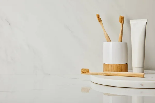 Round board with toothpaste in tube, holder and bamboo toothbrushes on white marble background — Stock Photo