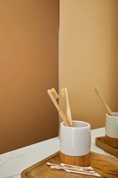 Placa com escovas de dentes de bambu em suporte, auriculares e espelho na mesa de mármore branco e fundo bege — Fotografia de Stock