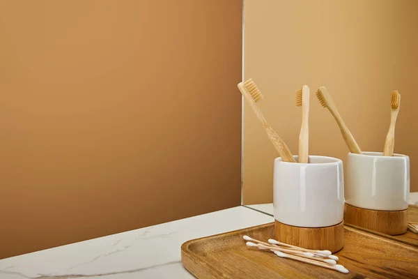 Placa de madeira com escovas de dentes de bambu em suporte e auriculares besidemirror na mesa branca e fundo bege — Fotografia de Stock