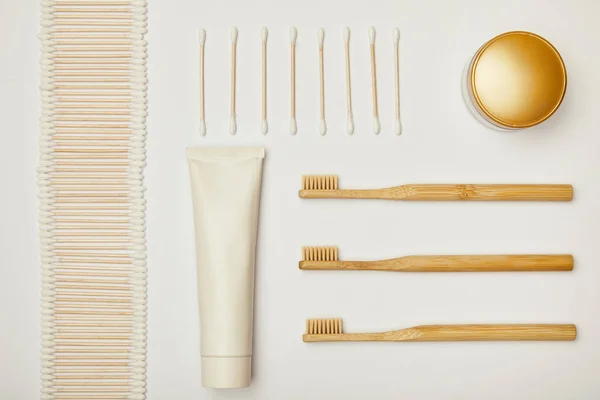 Top view of laid out ear sticks, toothpaste in tube, cosmetic cream and toothbrushes on white background — Stock Photo