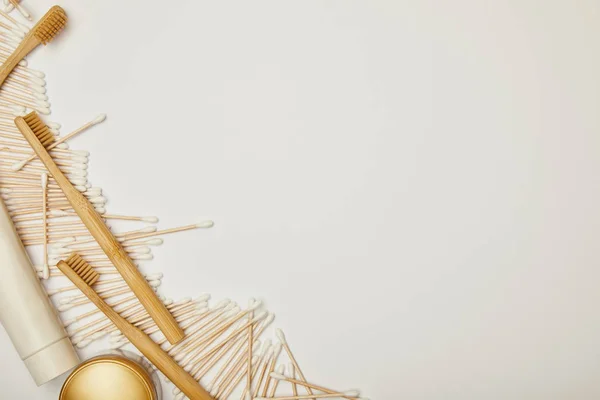 Vista dall'alto di auricolari, dentifricio in tubo, crema cosmetica e spazzolini di bambù su sfondo bianco — Foto stock