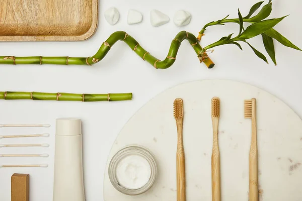 Vista superior de auriculares, pasta de dentes em tubo, creme cosmético, escovas de dentes e hastes de bambu no fundo branco — Fotografia de Stock