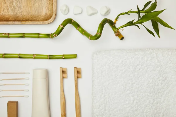 Top view of towel, ear sticks, toothpaste in tube, cosmetic cream, toothbrushes, stones and bamboo stem on white background — Stock Photo