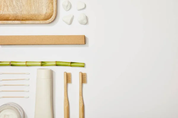 Vista superior de escovas de dentes de bambu, pasta de dentes em tubo, creme cosmético, pedras, auriculares e haste de bambu no fundo branco — Fotografia de Stock