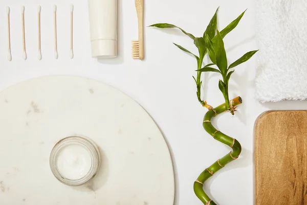 Vue du dessus du panneau rond en marbre avec crème cosmétique et brosse à dents, et dentifrice en tube, bâtons d'oreille, tige de bambou et serviette sur fond blanc — Photo de stock