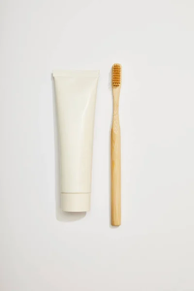 Vista superior de la pasta de dientes de bambú en tubo y cepillo de dientes sobre fondo blanco - foto de stock