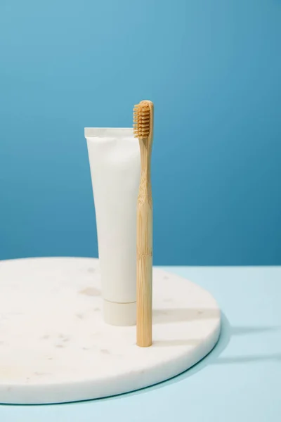 Placa redonda de mármore branco com pasta de dentes de bambu em tubo e escova de dentes no fundo azul — Fotografia de Stock