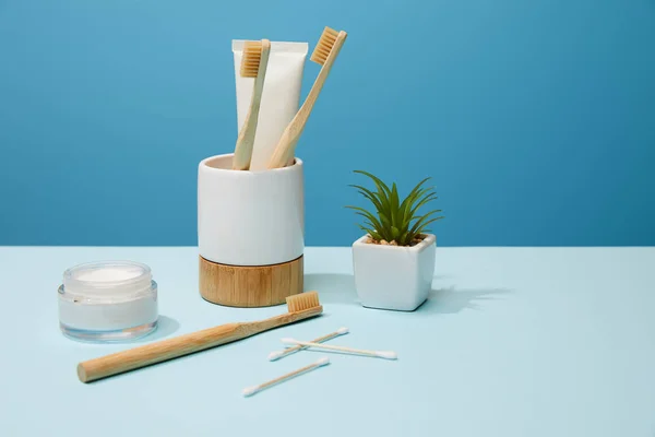 Holder for toothbrushes, cosmetic cream and plant in pot on table and blue background — Stock Photo