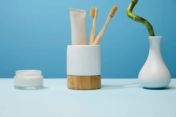 Suporte para escovas de dentes, creme cosmético e haste de bambu na mesa e fundo azul — Fotografia de Stock