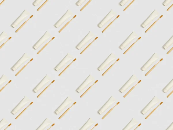 Cepillos de dientes de bambú ubicados en diagonal y pasta de dientes en tubos sobre fondo gris, patrón de fondo sin costuras - foto de stock