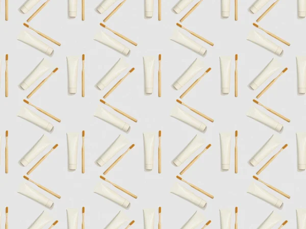 Bamboo toothbrushes and toothpaste in tubes in different directions on grey background, seamless background pattern — Stock Photo