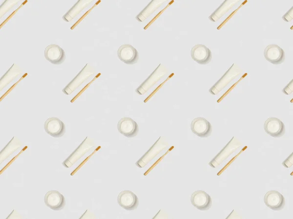 Diagonally located bamboo toothbrushes, toothpaste in tubes and cosmetic cream on grey background, seamless background pattern — Stock Photo