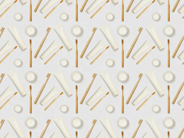 Bamboo toothbrushes, toothpaste in tube in different directions and cosmetic cream on grey background, seamless background pattern — Stock Photo