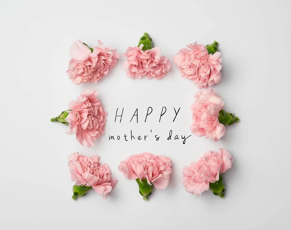 Vista superior del marco floral hecho de claveles rosados sobre fondo blanco con letras felices del día de las madres - foto de stock