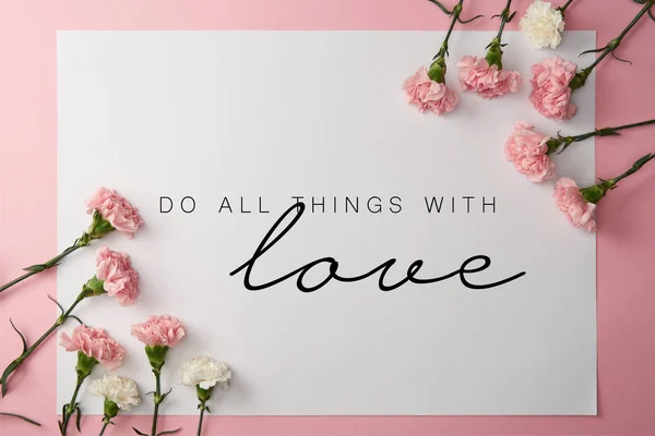 Vue du dessus des fleurs d'oeillet rose et blanc et carte avec faire toutes choses avec l'amour lettrage sur fond rose — Photo de stock