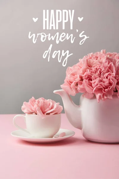 Fleurs oeillet rose en tasse et théière sur fond gris avec lettrage heureux jour des femmes — Photo de stock