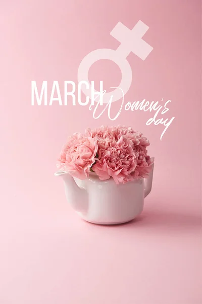 Flores de clavel rosa en tetera blanca sobre fondo rosa con letras de día para mujer - foto de stock