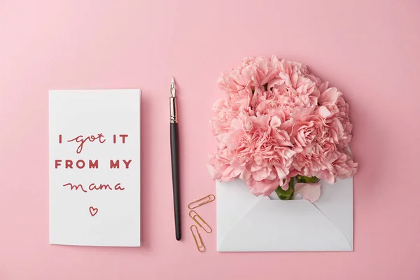 Vista superior do dia das mães cartão de saudação e envelope com cravos no fundo rosa — Fotografia de Stock