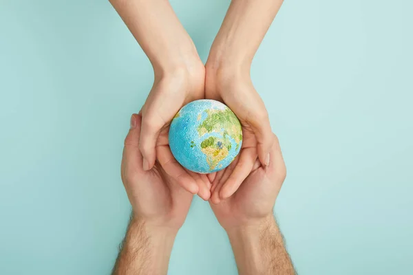 Вид сверху на мужчину и женщину, держащих модель планеты на бирюзовом фоне, концепция Дня Земли — стоковое фото
