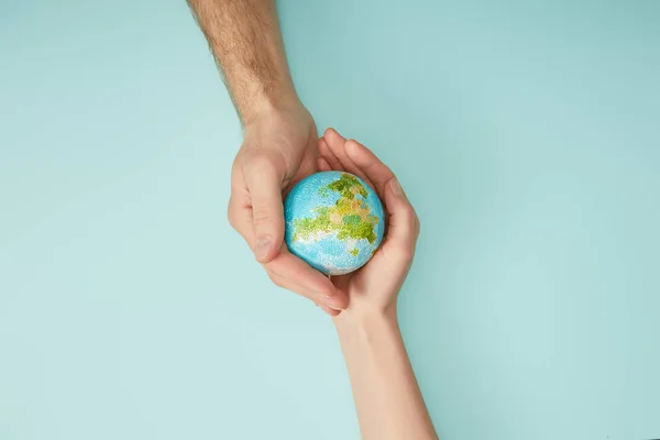 Top view of man and woman holding planet model on turquoise background, earth day concept — Stock Photo