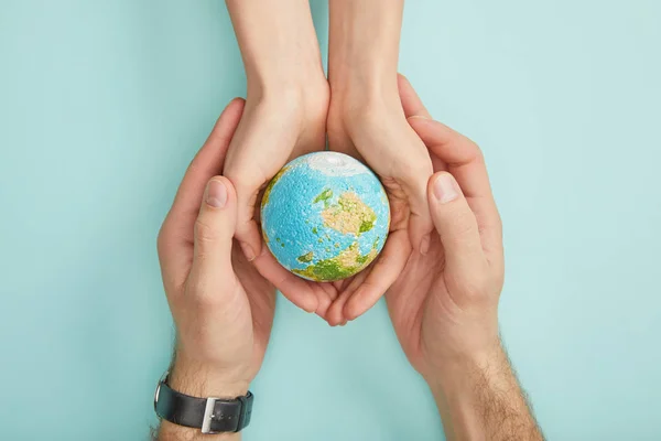 Top view of man and woman holding planet model on turquoise background, earth day concept — Stock Photo