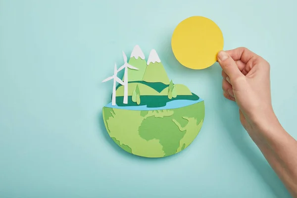 Draufsicht auf Frau mit Papier geschnittener Sonne und Planet mit erneuerbaren Energiequellen auf türkisfarbenem Hintergrund, Earth Day Konzept — Stockfoto