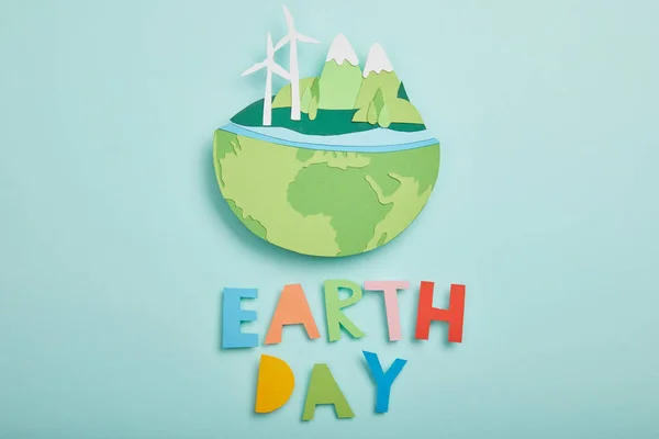 Vista superior del planeta cortado en papel con fuentes de energía renovables y coloridas letras de papel sobre fondo turquesa, concepto del día de la tierra - foto de stock