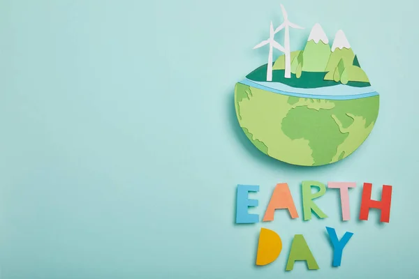 Draufsicht auf Papier geschnittenen Planeten mit erneuerbaren Energiequellen und bunten Buchstaben auf türkisfarbenem Hintergrund, Earth Day Konzept — Stockfoto