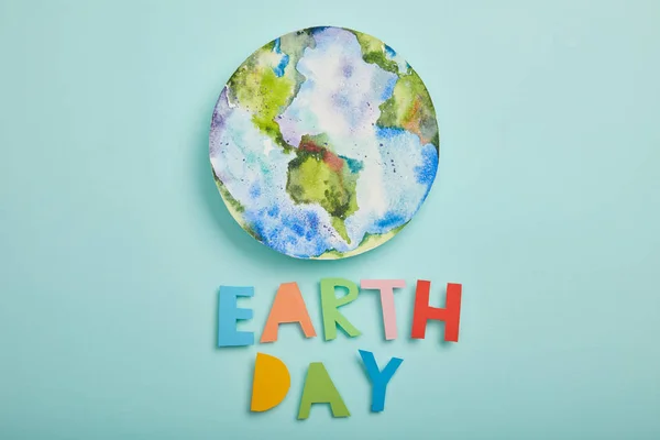 Draufsicht auf bunte Papierbuchstaben und Planetenbild auf türkisfarbenem Hintergrund, Earth Day Konzept — Stockfoto