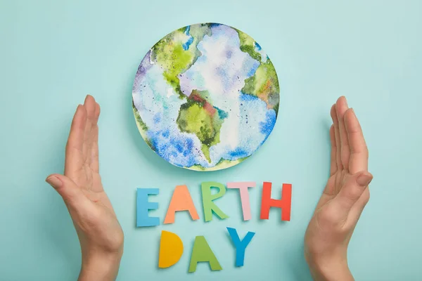 Draufsicht der Frau mit bunten Papierbuchstaben und Planetenbild auf türkisfarbenem Hintergrund, Earth Day Konzept — Stockfoto