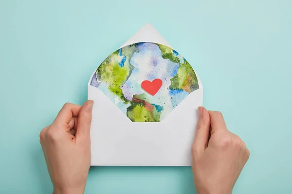 Top view of woman holding envelope with planet picture on turquoise background, earth day concept — Stock Photo