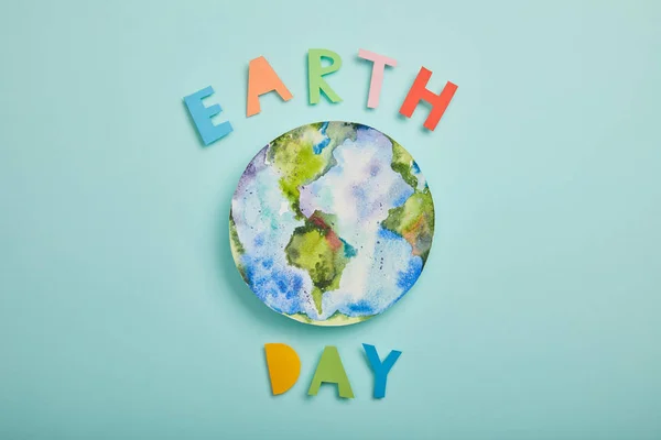 Vista superior de las letras de papel de colores y la imagen del planeta sobre fondo turquesa, concepto del día de la tierra - foto de stock