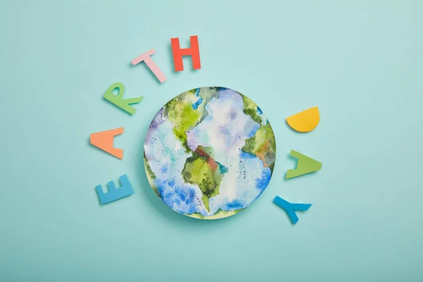 Vista superior de las letras de papel de colores y la imagen del planeta sobre fondo turquesa, concepto del día de la tierra - foto de stock