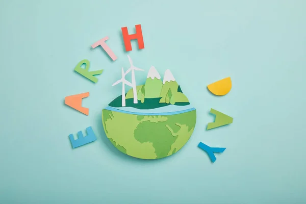 Draufsicht auf Papier geschnittenen Planeten mit erneuerbaren Energiequellen und bunten Papierbuchstaben auf türkisfarbenem Hintergrund, Earth Day Konzept — Stockfoto